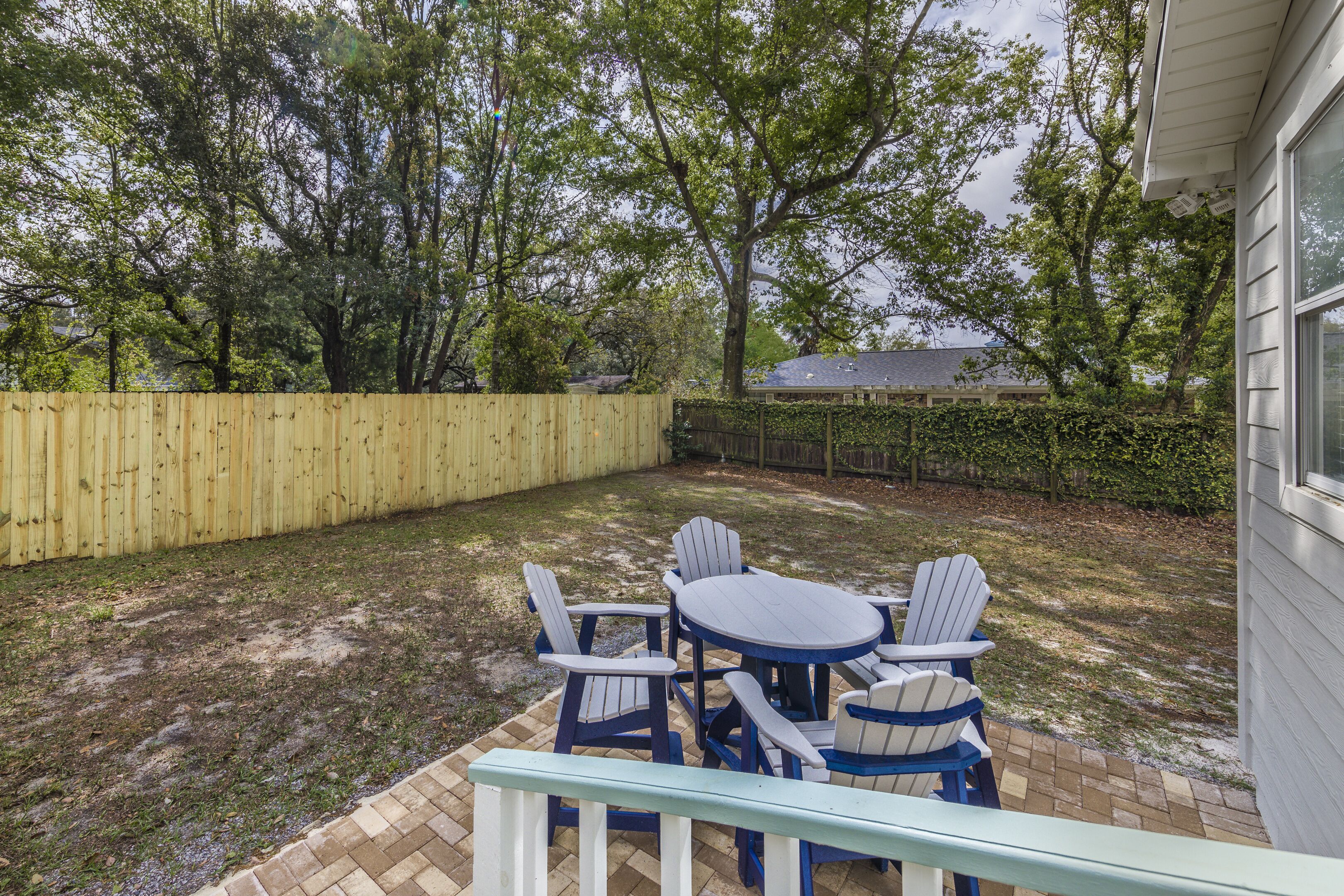 Un jardin avec une clôture en bois, une terrasse en briques et une table entourée de chaises.