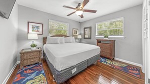 A bedroom with a bed, a ceiling fan, a nightstand, a dresser, and a window with blinds.