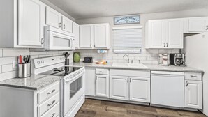 A kitchen with white cabinets, a stove, a dishwasher, and a coffee maker.