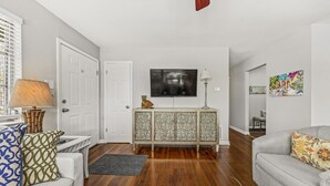 A living room with a white sofa, a grey sofa, a wooden coffee table, a cabinet, and a television.