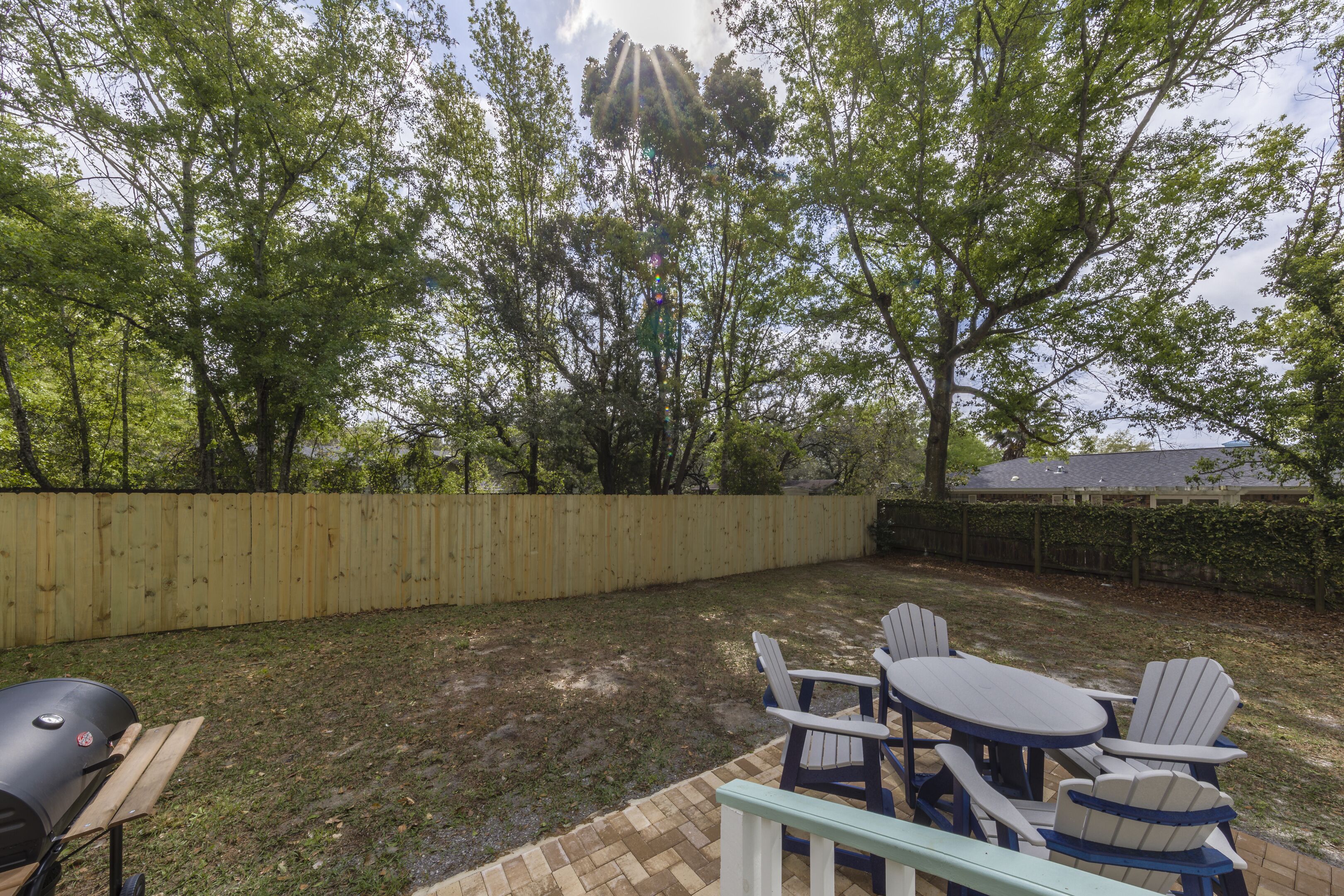 A backyard with a wooden fence, a barbecue grill, and a table with chairs.