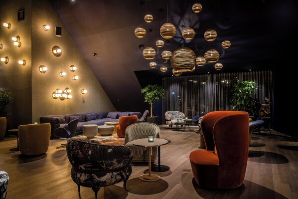 Un área de estar moderna con diversas opciones de asiento, incluyendo sofás y sillones, una mesita redonda y una planta en maceta.