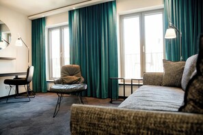 A hotel room with a bed, a chair, a desk, and a large window with curtains.