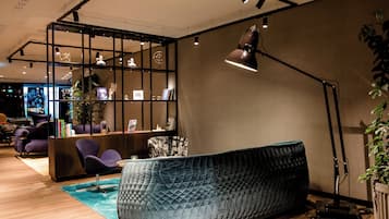 Ein moderner Empfangsbereich mit einem blauen Sofa, einem schwarzen Schreibtisch und einer Regalanlage mit Büchern und Dekoration.
