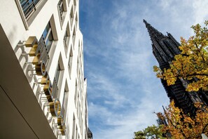 A modern building with a geometric facade and a gothic spire in the background.