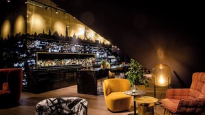 A bar area with a city skyline view, bar counter, seating area with chairs, and a potted plant.