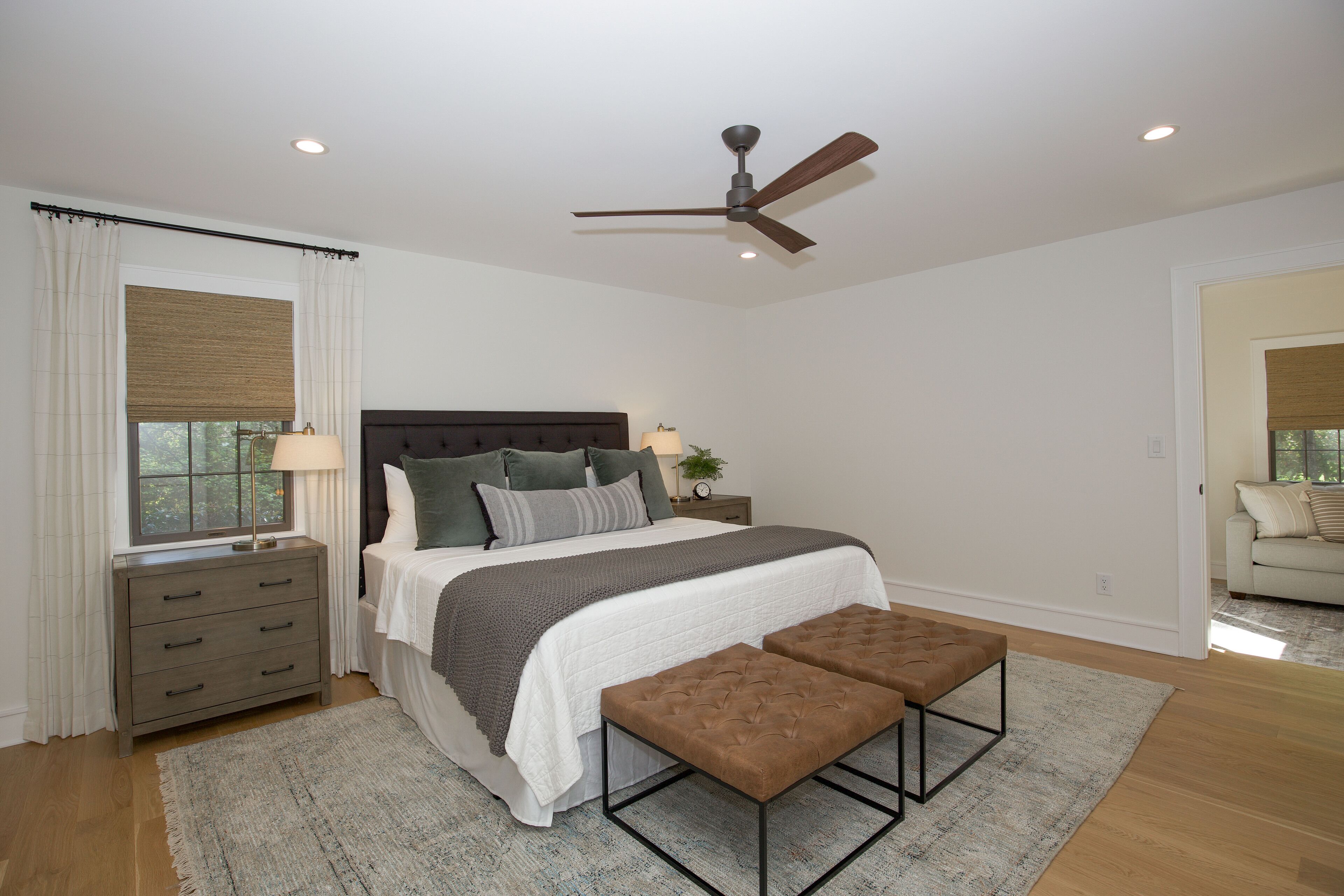 A bedroom with a bed, bedside tables, a ceiling fan, and a window with curtains.