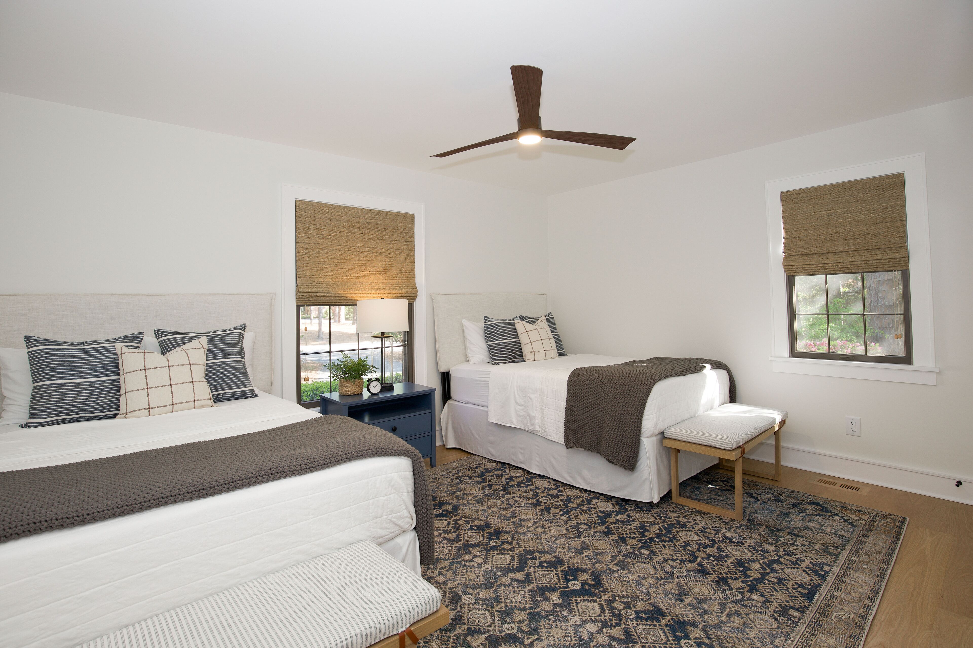 Une chambre avec deux lits, un ventilateur de plafond et un tapis à motifs.