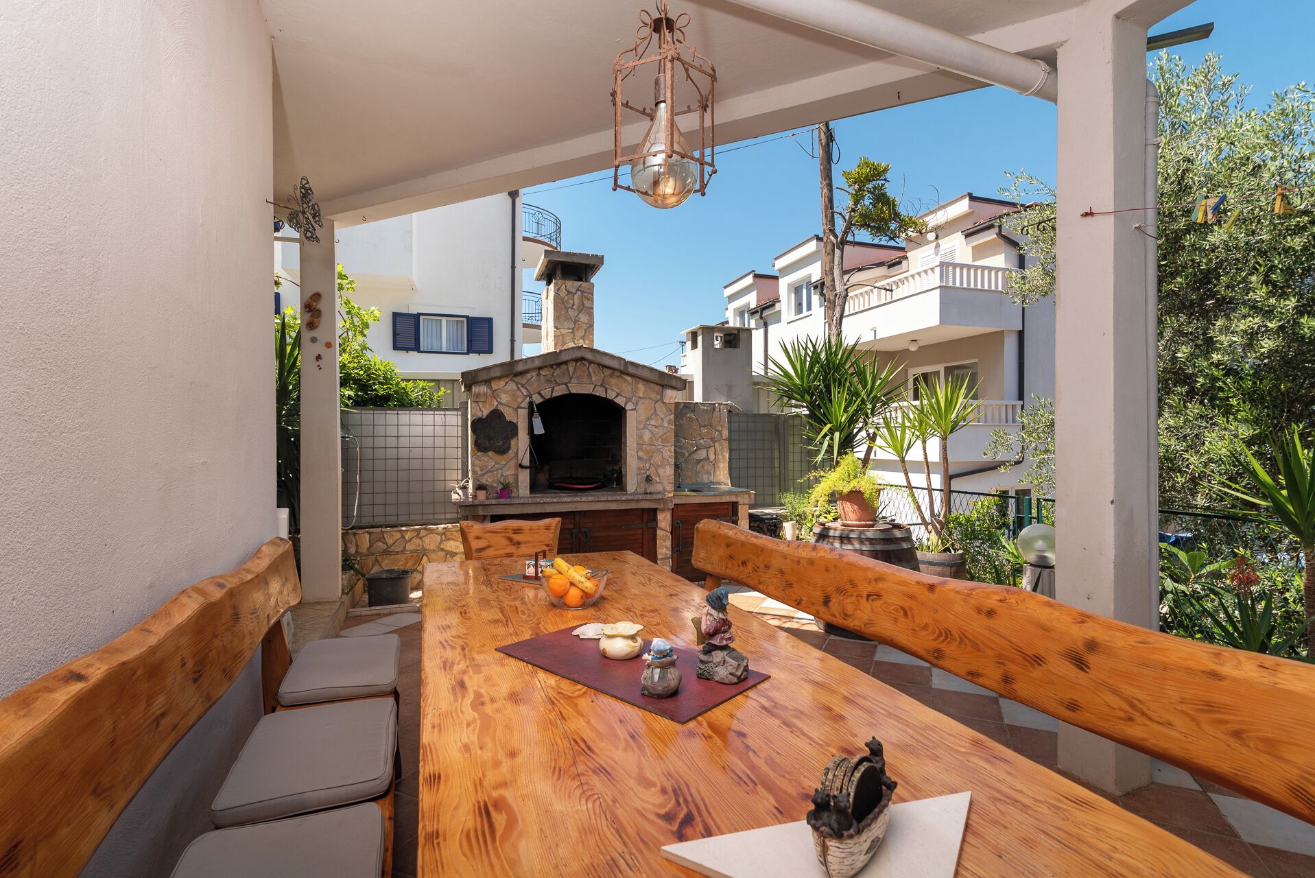 An outdoor dining area with a stone-built pizza oven, wooden benches, and a view of neighboring buildings.