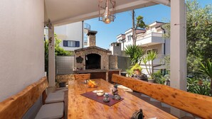 An outdoor dining area with a stone-built pizza oven, wooden benches, and a view of neighboring buildings. - MARIC 1 apt for 4+2, only 40 m from the beach in Mastrinka (Mastrinka)