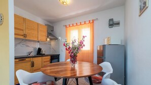 A compact kitchen with wooden cabinets, a marble countertop, a dining table with white chairs, and a refrigerator. - MARIC 1 apt for 4+2, only 40 m from the beach in Mastrinka (Mastrinka)