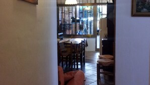 Ein Blick ins Innere eines Essbereichs mit einem Tisch, Stühlen, einer hängenden Pflanze und einem Gemälde an der Wand.