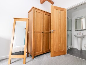 A wooden wardrobe with a mirror and a door, a white sink, and a shower area in a bathroom. - 11 Towan Valley (Truro)