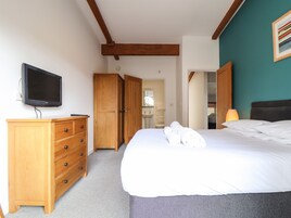 Un dormitorio con cama, cómoda de madera, televisor y baño visible a través de una puerta abierta.