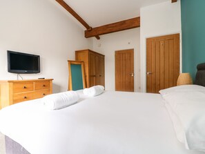 A bedroom with a large bed, wooden wardrobe, a television, and a teal-colored door. - 11 Towan Valley (Truro)