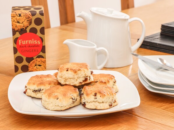 Un plato de scones, una jarrón blanco y una caja de scones de jengibre y chocolate oscuro.