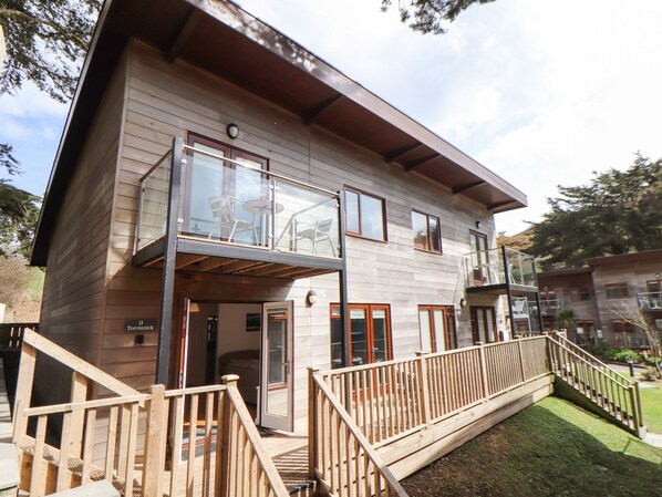 A two-story wooden building with a balcony, a staircase, and a small outdoor seating area. - 11 Towan Valley (Truro)