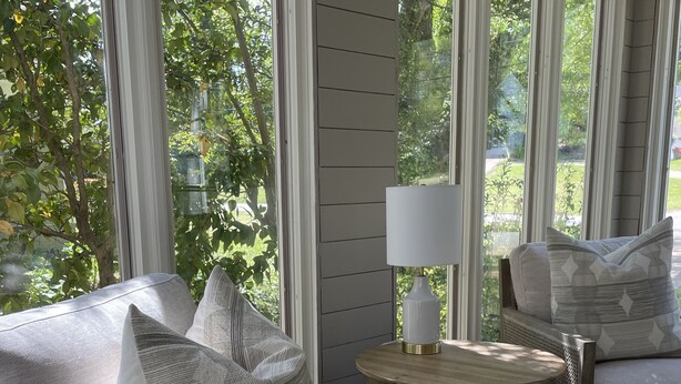 A sunlit room with a wicker sofa, a round wooden table, and a lamp.