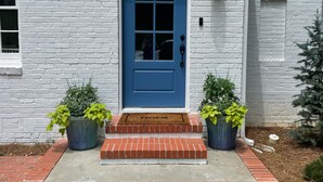 A white brick building with a blue door, numbered 502, and two potted plants on the front steps.