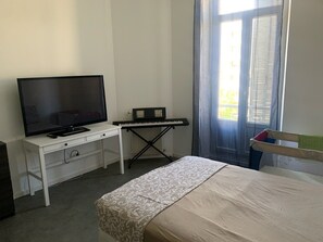 Ein Schlafzimmer mit einem Bett, einem Fernseher, einem Klavier und einem Fenster mit Vorhängen.