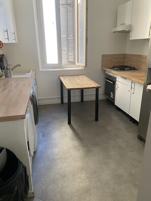 Eine kleine Küche mit Fenster, einer Waschmaschine, einem Tisch und einem Herd.