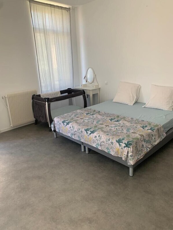 Ein Schlafzimmer mit einem Bett, einem kleinen Nachttisch mit Spiegel, einem Fenster mit Vorhängen und einer Heizung.