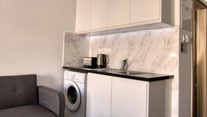 A compact kitchen with a washing machine, a coffee maker, and a microwave. - Phaedrus Living Seaside Luxury Flat Athina 118 (Paphos)