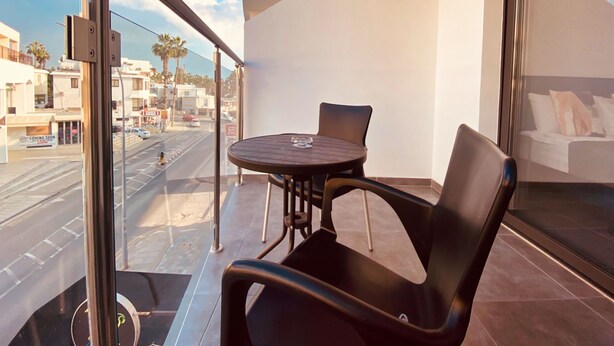 A balcony with a table and chairs, a view of the street, and a bed in the adjacent room. - Phaedrus Living Seaside Luxury Flat Athina 118 (Paphos)