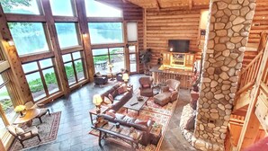 A spacious log cabin interior with large windows, a stone pillar, and a cozy seating area. - River Ridge Lodge: Luxury Lodge on the Menominee River (Stephenson)