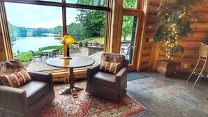 A cozy room with two leather armchairs, a round table, and a view of a lake through large windows. - River Ridge Lodge: Luxury Lodge on the Menominee River (Stephenson)