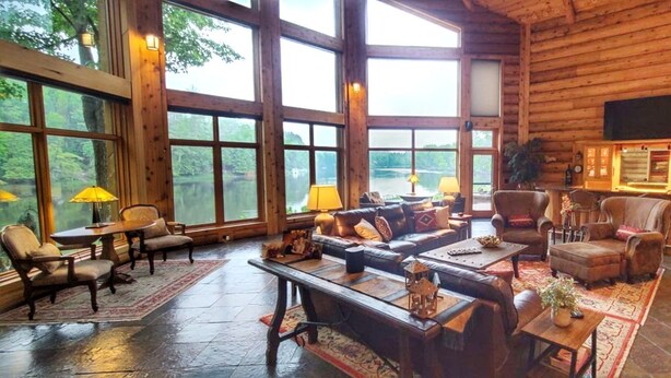 A spacious log cabin interior with large windows, a fireplace, and a cozy seating area. - River Ridge Lodge: Luxury Lodge on the Menominee River (Stephenson)