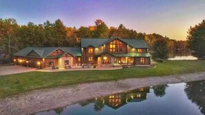 A large log cabin with multiple rooms, a porch, and a reflection in the water. - River Ridge Lodge: Luxury Lodge on the Menominee River (Stephenson)