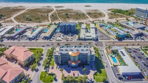 Eine Luftaufnahme eines Küstenhotels mit mehreren Gebäuden, einem zentralen Bauwerk mit gewölbter Dachlinie und einem Strand im Hintergrund.
