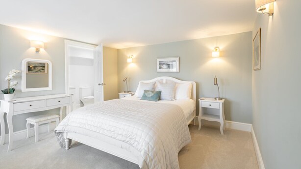 A bedroom with a bed, bedside tables, a dresser, a mirror, and wall-mounted lights.