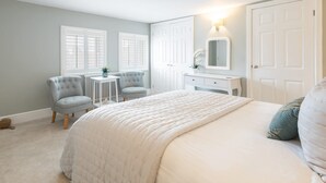 A bedroom with a large bed, two armchairs, a small table, a dresser, and a mirror.
