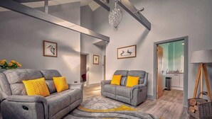 A modern living room with two grey sofas, yellow cushions, and a chandelier. - Host & Stay | Bluebell Cottage (Belford)