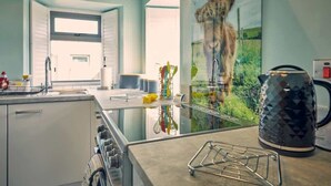 A modern kitchen with a large window, a kettle, and a view of a lion. - Host & Stay | Bluebell Cottage (Belford)