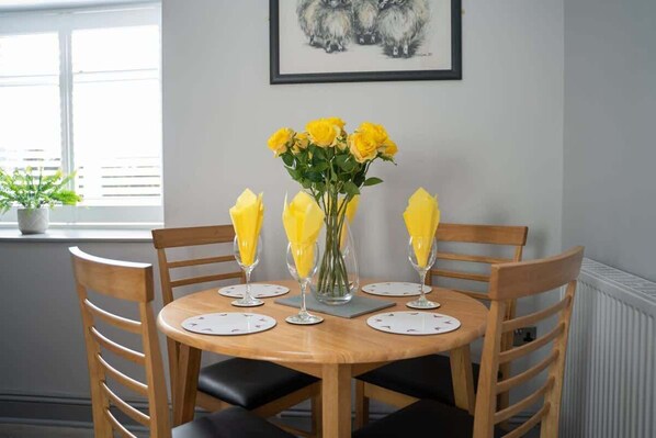 A dining table set with yellow flowers in a vase, surrounded by wooden chairs with black cushions.