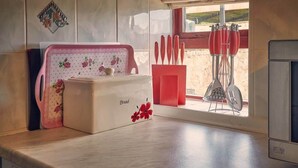 Un plan de travail de cuisine avec un boîtier à pain, un porte-couteaux rouge et une fenêtre donnant sur l’extérieur.