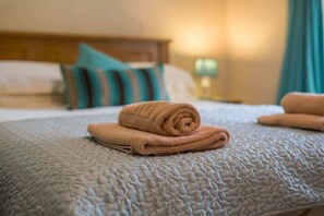 A neatly made bed with a textured grey bedspread and two rolled towels on top. - Host & Stay | No.5 Poppy Cottage (Belford)