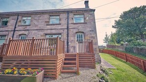 A two-story stone building with a wooden deck and a flower bed.