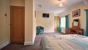 A bedroom with a bed, a desk, a chair, a door, and a ceiling light.