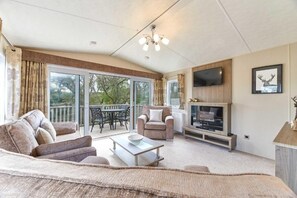 Een ruime woonkamer met een bank, salontafel en een open haard. Er is een televisie aan de muur bevestigd en een balkon met tuinmeubilair.