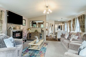 A modern living room with a flat-screen TV, a dining area, and a kitchen. - Host & Stay | Sammy's Retreat (Felton)