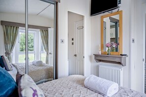 A bedroom with a bed, a mirror, a television, and a view of the outdoors.