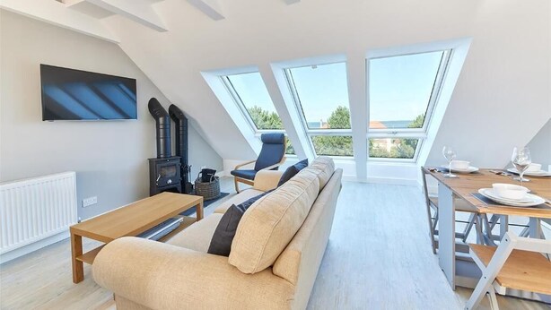 Een modern loft appartement met een groot dakvenster, een bank, een eettafel gedekt voor twee personen en een open haard.