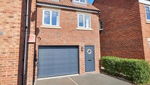 Een tweelaags bakstenen huis met garage, een kleine voortuin en een helderblauwe lucht.