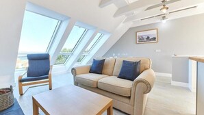 Een moderne woonkamer met een bank, fauteuil en tafel. Er zijn dakramen en een plafondventilator.