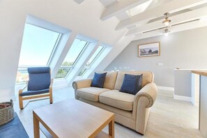 Un salon moderne avec un canapé, un fauteuil et une table. Il y a des fenêtres de toit et un ventilateur de plafond.