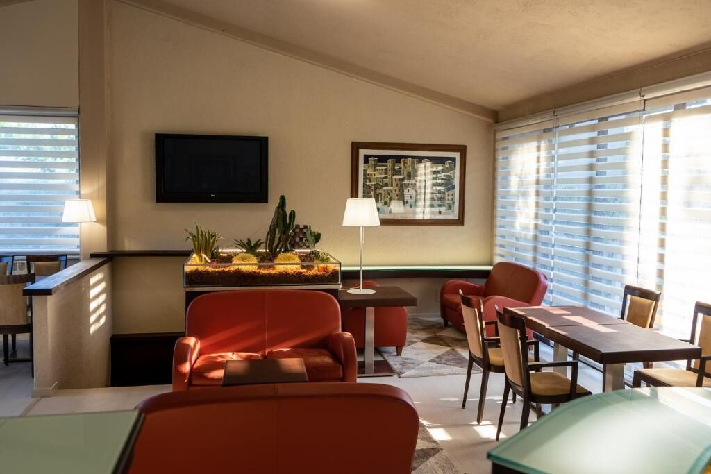 Camera d'albergo con divano, tavolo da pranzo con sedie, televisore a parete e finestra con tende.